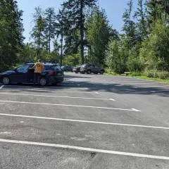 Parking przy szlaku na przełęcz Szarcula. Kilka samochodów na nowym, asfaltowym parkingu otoczonym lasem.