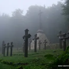 Mglisty poranek na cmentarzu wojennym na Magurze Malastowskiej. Drewniane krzyże stoją w szeregach, a w tle wznosi się monumentalny pomnik.