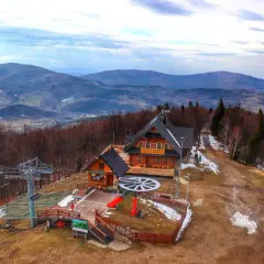 Drewniana chata i kolejka linowa na Mosornym Groniu. W tle malownicze, zalesione wzgórza Beskidu.