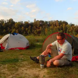 Mężczyzna przygotowuje posiłek podczas obozowania w namiotach nad jeziorem.
