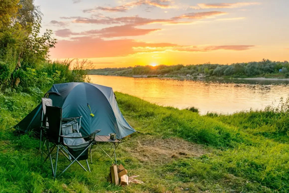 Namiot, krzesła i stolik czekają na nocleg. Piękny zachód słońca nad rzeką, idealny na **camping w lesie**.